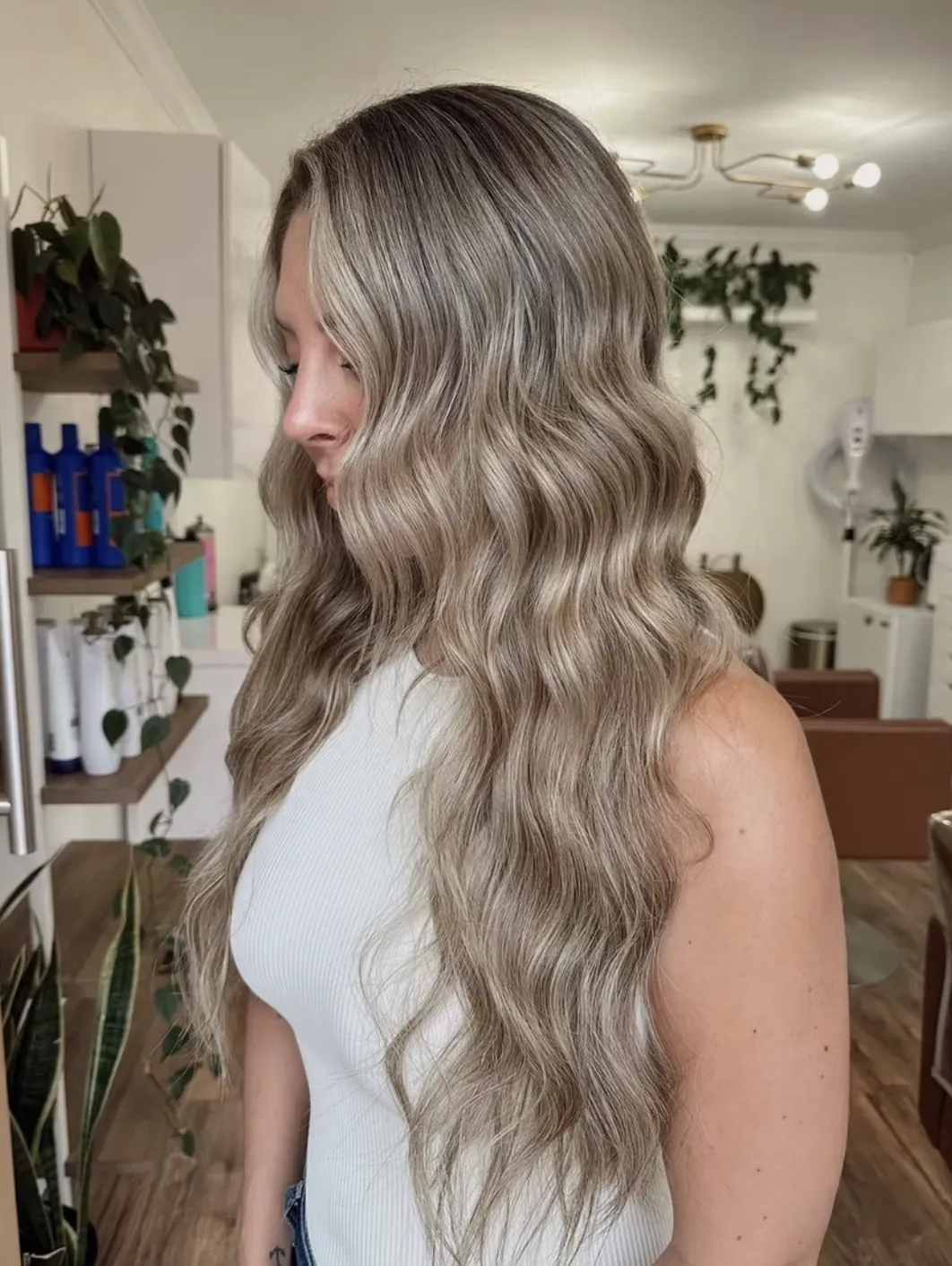 Long ash blonde balayage styled in soft waves, showing blended cool tones and dimensional finish in a salon setting.