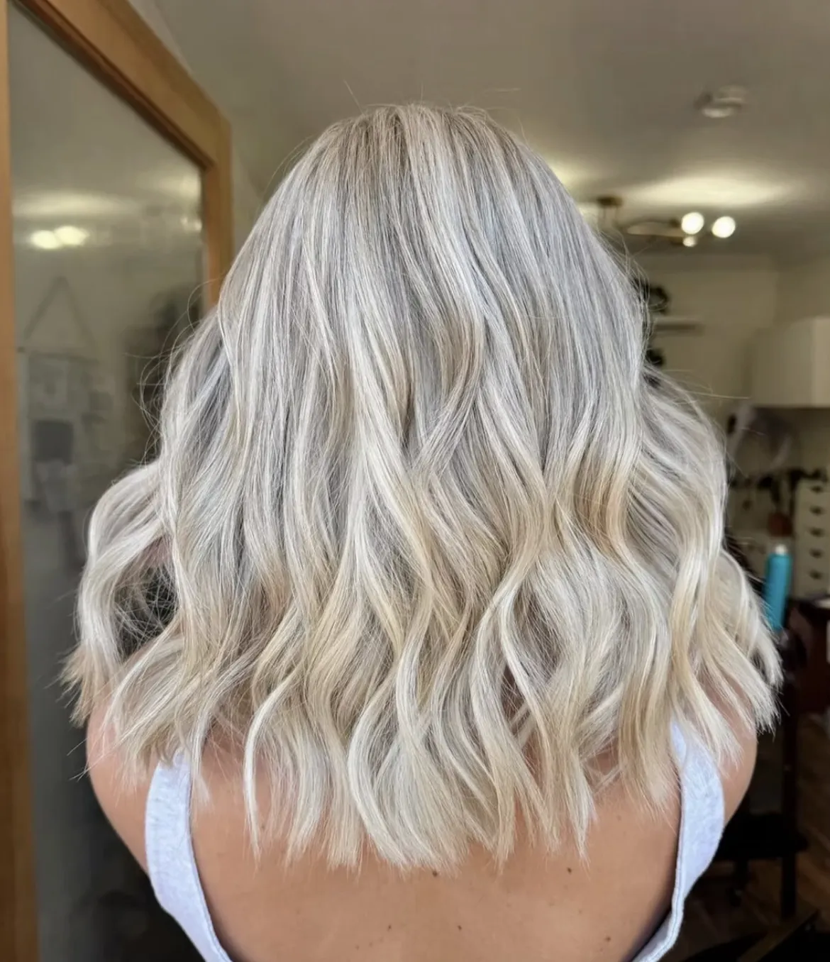 Shoulder-length platinum blonde balayage styled in soft waves, showing blended light tones and natural texture in a salon setting.