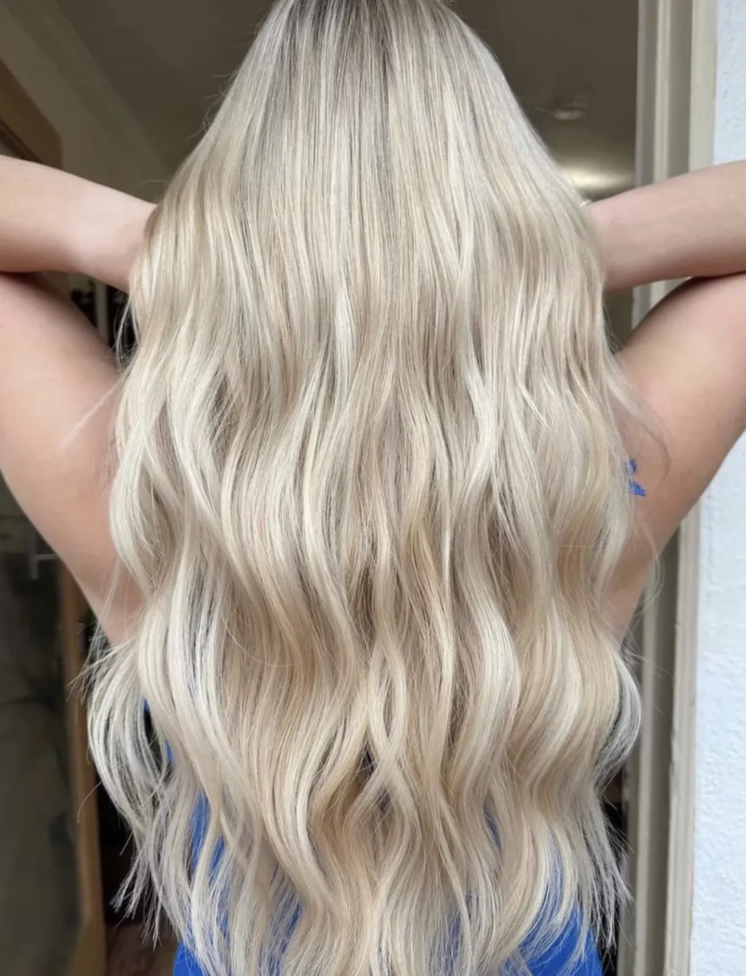 Long blonde balayage styled in soft natural waves, showing blended light tones and smooth finish in a professional setting.