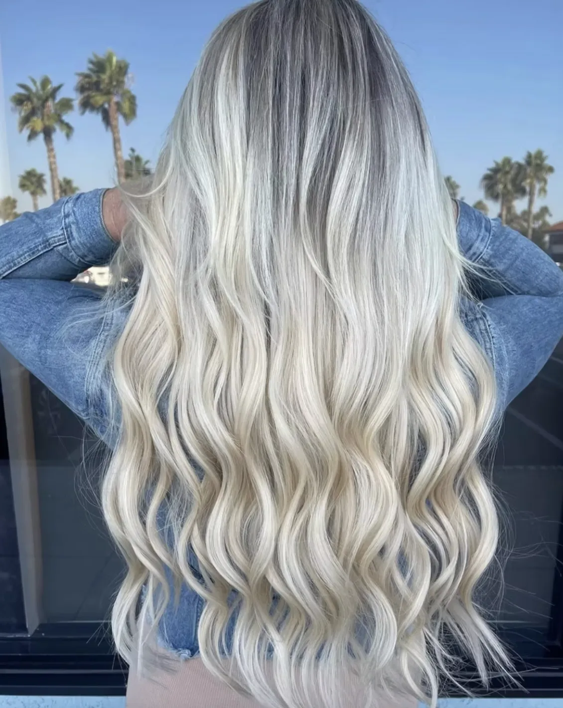 Long platinum blonde balayage styled in beach waves, showing blended light tones and smooth finish in an outdoor setting.