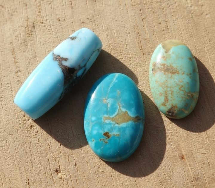 Close-up of three turquoise stones showing color, matrix, and shape differences. Natural linen or raw wood background. Warm, soft light.