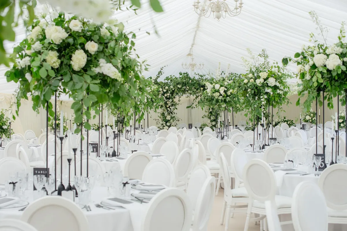 A marquee set for a wedding with Louis style white chairs and huge green and white floral designs.