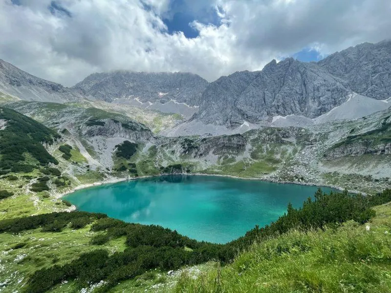 Turquoise mountain lake surrounded by dramatic alpine peaks, rocks, and lush greenery