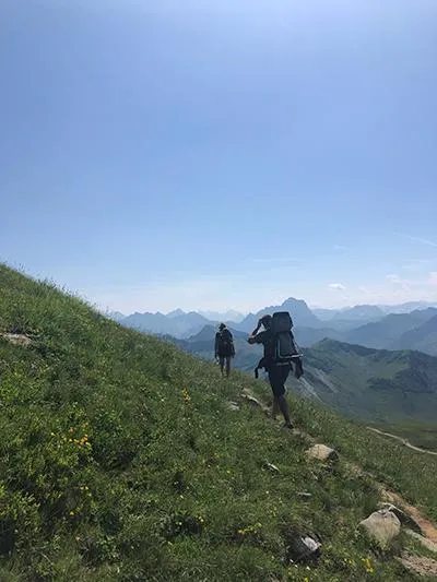 Family hiking in Austria on a green hillside with mountains in the background
