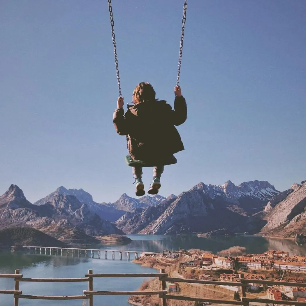 Boy enjoying a swing outdoors with scenic European mountains in the background