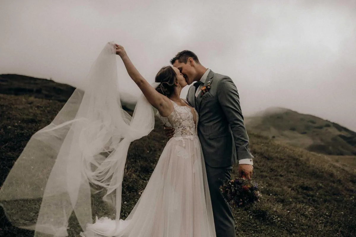 Bride and groom kissing while he holds her flowers