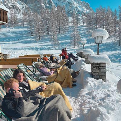 People relaxing in lounge chairs with blankets in snowy Alpine winter sun, enjoying a peaceful après-ski afternoon