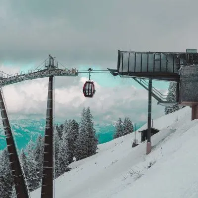 Gondola in snowy Alpine mountains nearing top station, with snow-covered trees and winter clouds in the background