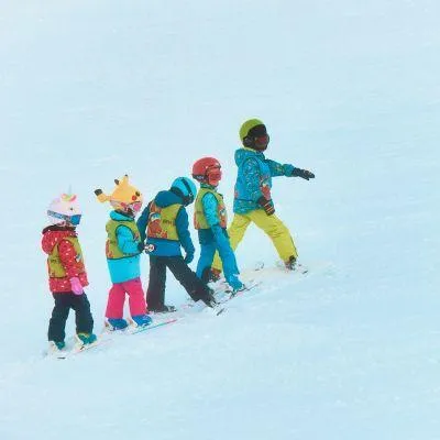 Kids ski school in the Alps with five children in ski gear learning to ski on a snowy slope