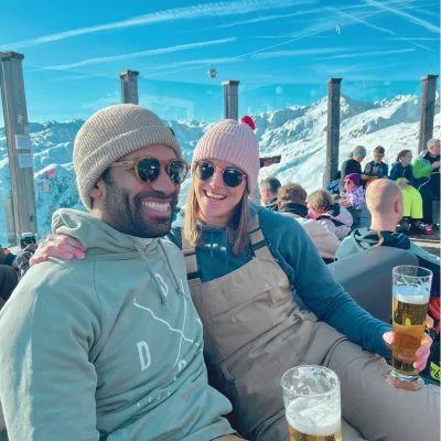 Couple enjoying beer at sunny Alpine après-ski hut with mountain views on a European ski trip