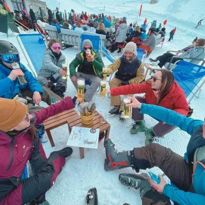 Friends in lounge chairs outside après-ski hut in the Alps, cheering with drinks and enjoying the winter sun