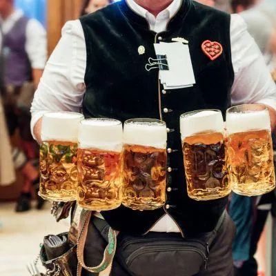 Oktoberfest waiter carrying five large Bavarian beers in a traditional beer tent, showcasing Munich’s Oktoberfest atmosphere and German beer culture.