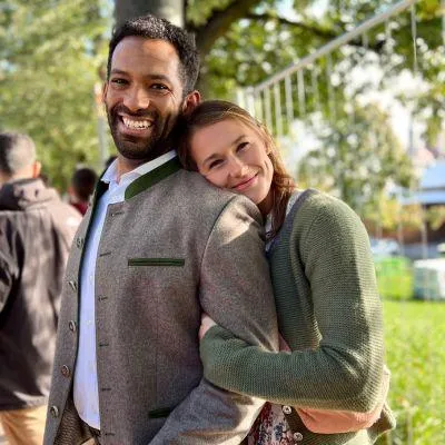 Man and woman in traditional Bavarian outfits at Oktoberfest Munich – wearing a Dirndl and Lederhosen in front of the festival grounds with beer tents and festive atmosphere in the background