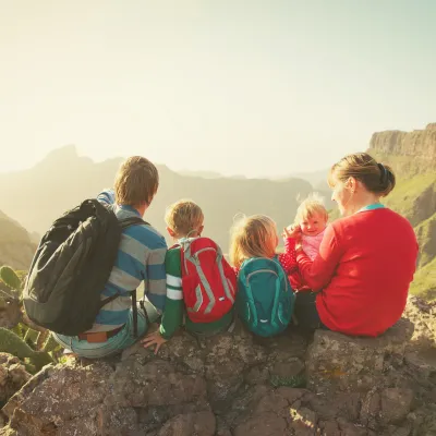 Mom, Dad and 3 small kids are sitting on a rock enjoying the views over the mountains