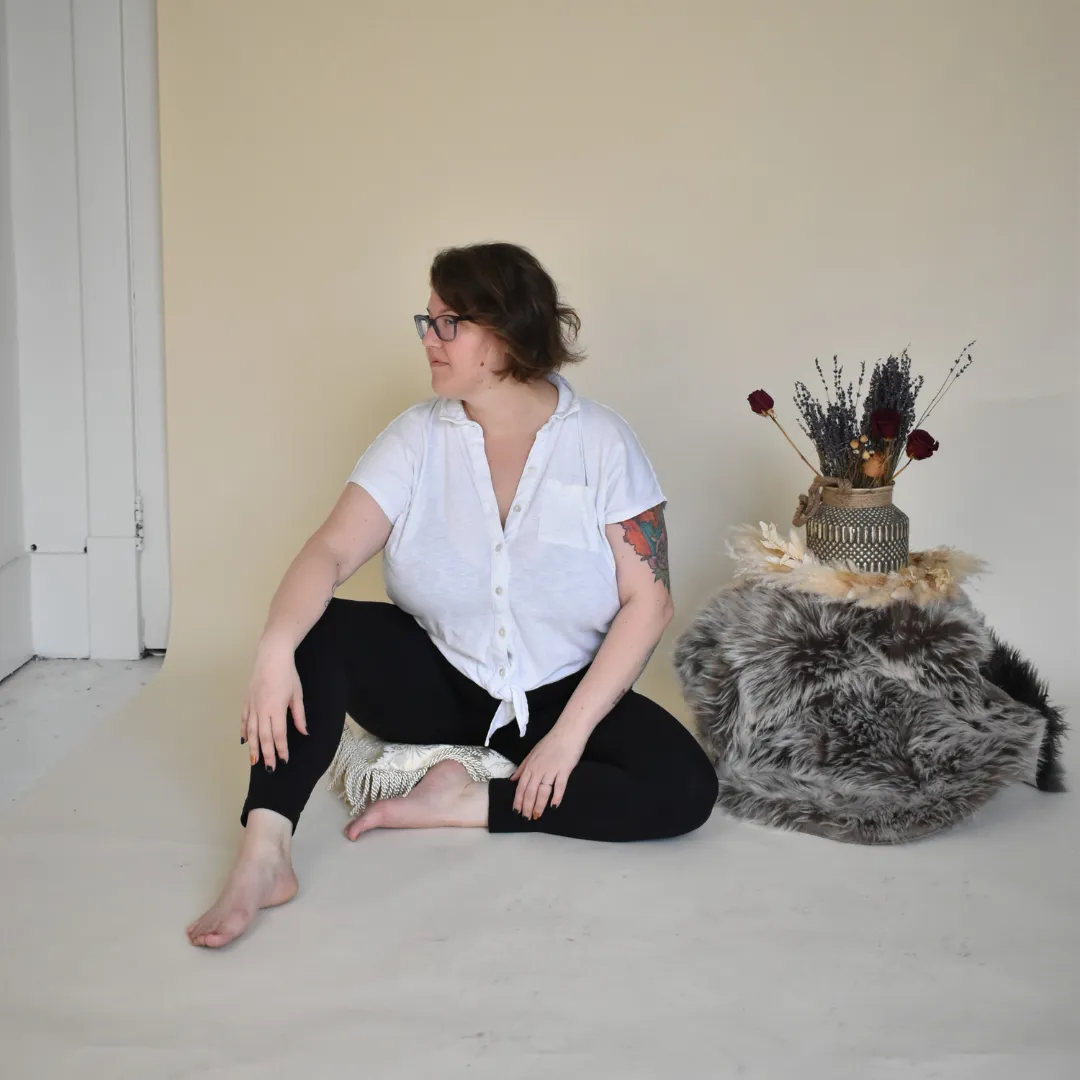 A person sitting on the floor one leg bent one tucked under. Looking to the left.