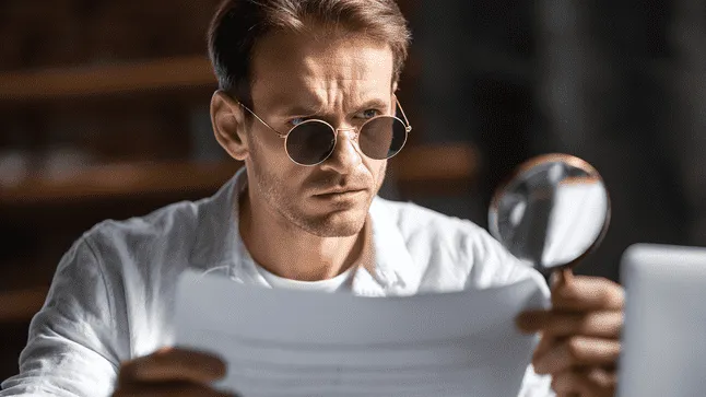 A business professional closely examines documents with a magnifying glass, representing preparation for a workers’ compensation audit, compliance review, and insurance documentation verification.