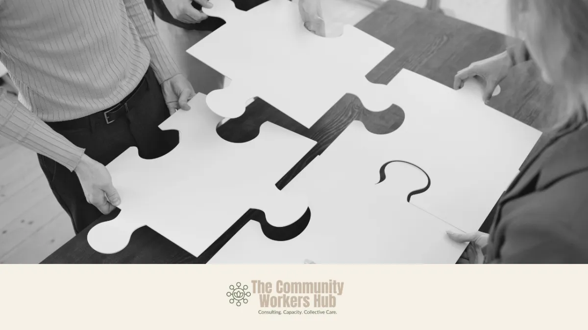 Several people stand around a table holding large white puzzle pieces, positioning them together to form a complete shape. The black-and-white image represents collaboration and collective problem-solving. The Community Workers Hub logo appears at the bottom of the image.