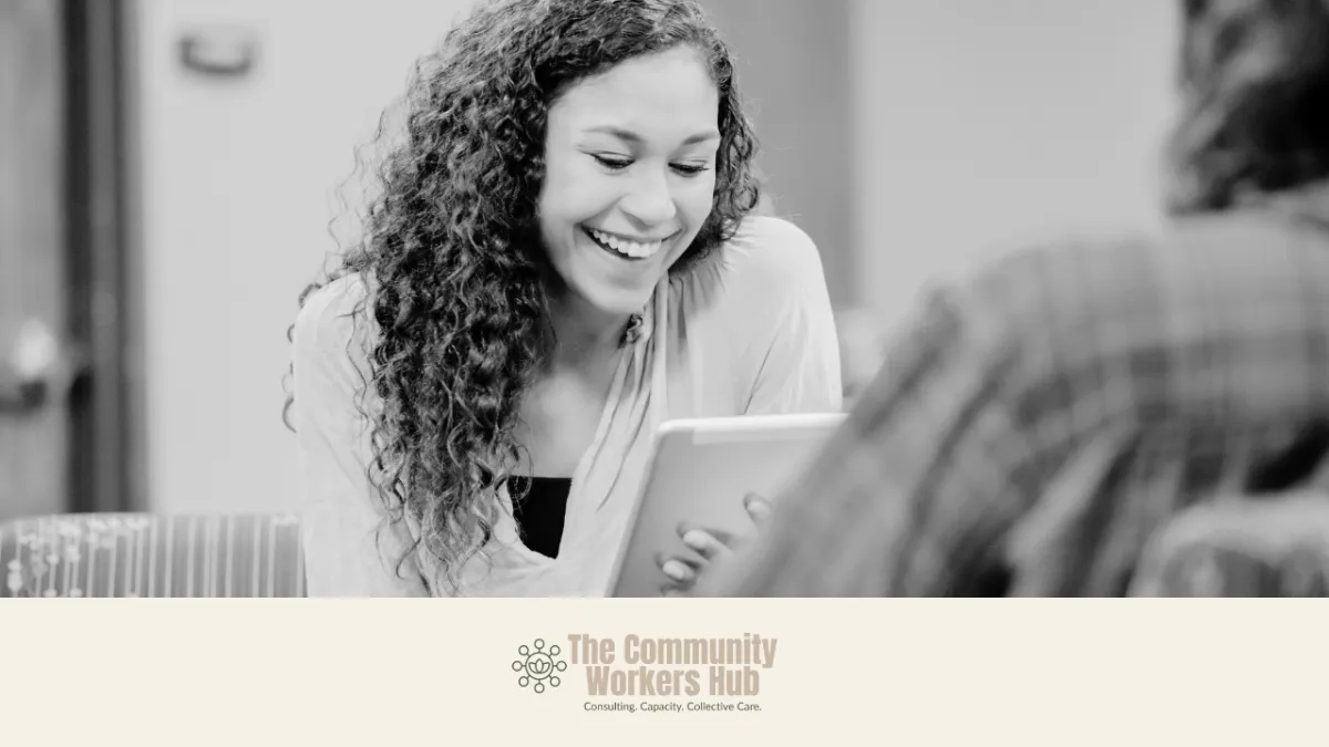 a black and white image os a woman smiling. She has long curly dark hair and is looking at a ipad. 