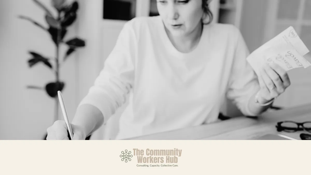 A person sits at a desk writing with a pen while holding paperwork in their other hand. The black-and-white image suggests focused planning or administrative work in a calm indoor setting. The Community Workers Hub logo appears at the bottom of the image.