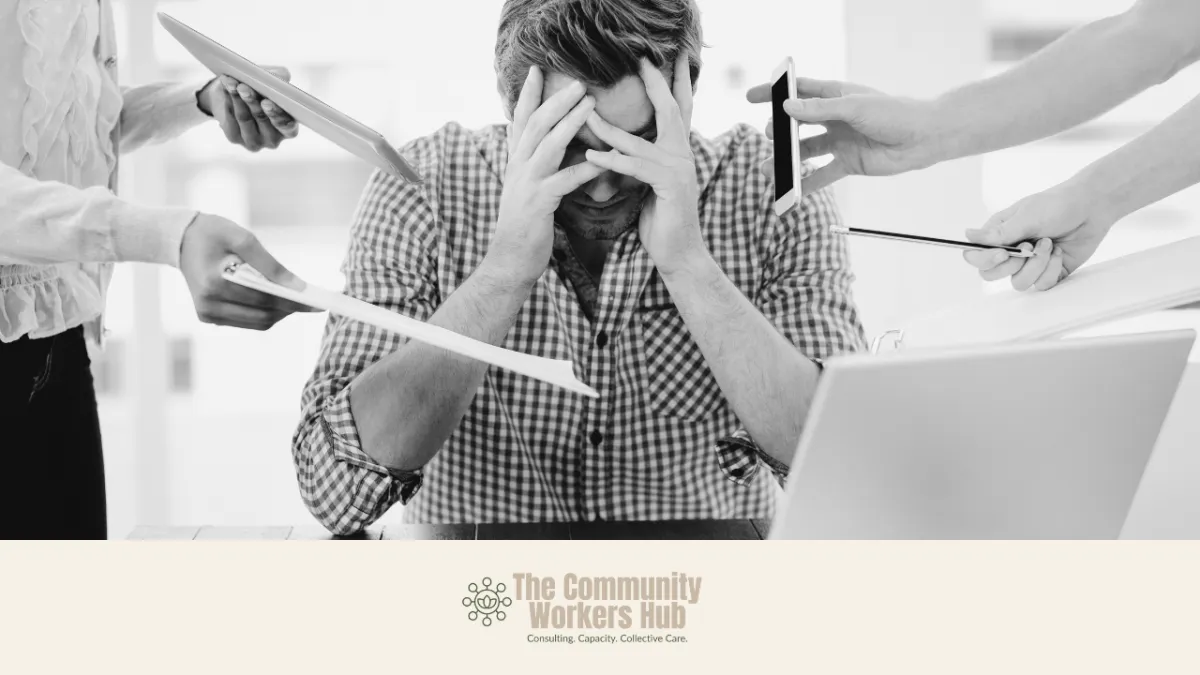 A man sits at a desk with his head in his hands, appearing overwhelmed, while multiple hands around him hold papers, a phone, a tablet, and a pen toward him. The black-and-white image conveys pressure, overload, and the need for de-escalation or support in a work or service context. The Community Workers Hub logo appears at the bottom of the image.