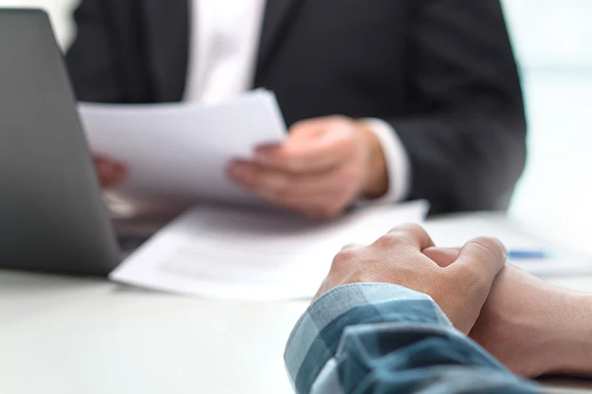 mans hands clasped as a money lender looks at papers and laptop