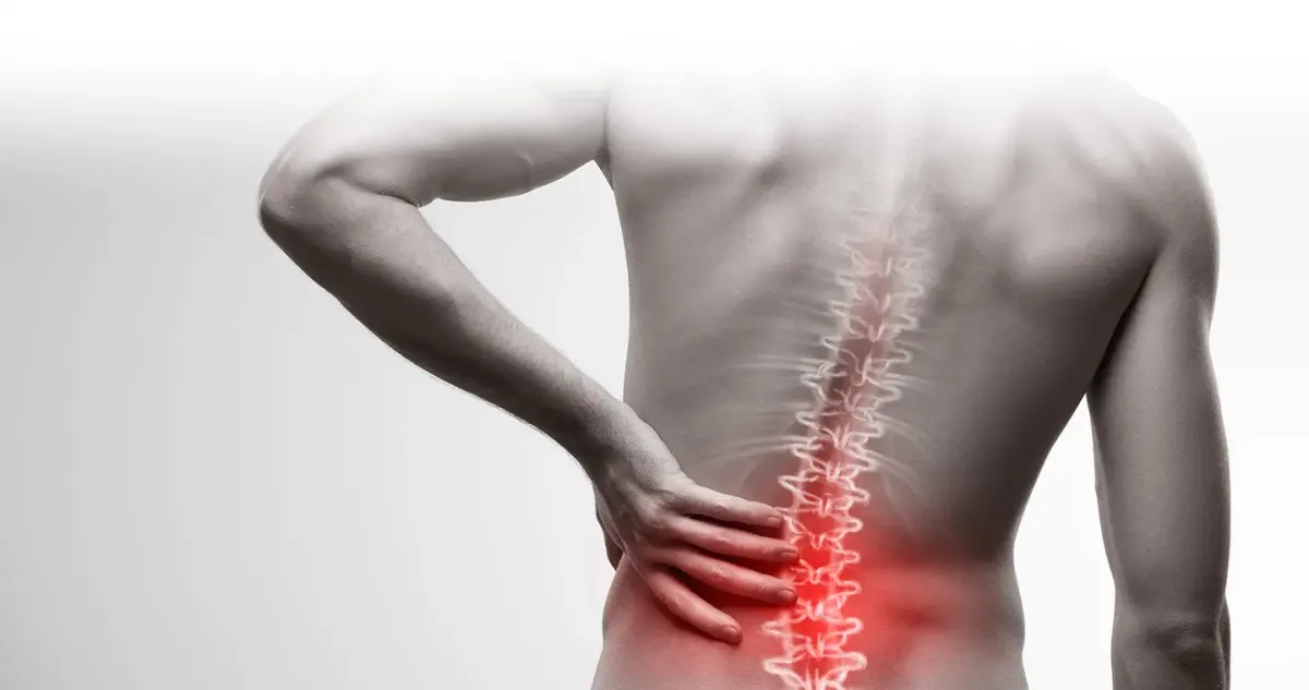 Person clutching their lower back in discomfort, symbolizing the common struggle with low back pain and the need for effective treatment.