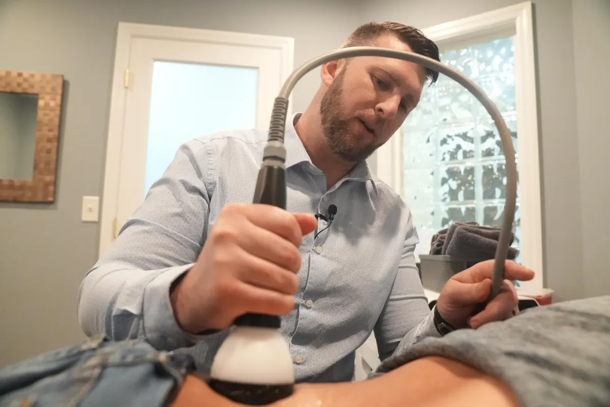 Dr. Matthew T. Jacobs performing StemWave therapy on a patient's arm using a specialized device. The treatment is aimed at promoting healing and reducing pain through acoustic sound waves, part of a comprehensive approach to nerve regeneration.