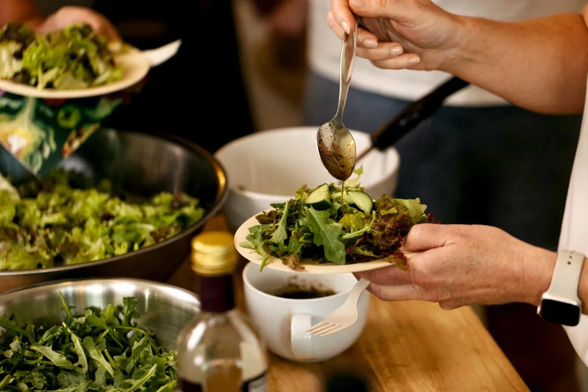 Guest adding homemade dressing to a fresh seasonal salad during gut health workshop demo