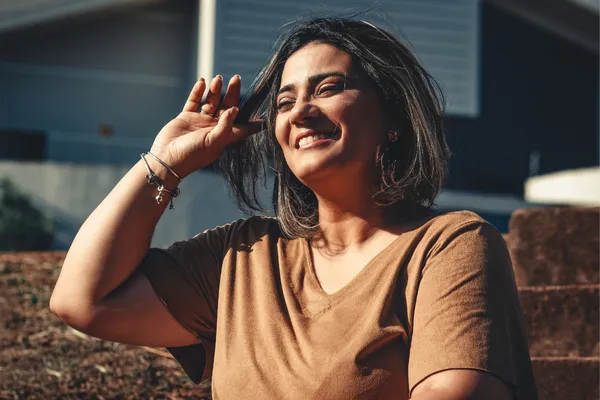 A midlife woman with glowing skin and a joyful expression, under sunlight.