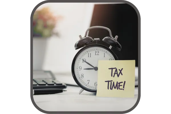 Tax time post it stuck on alarm clock on desk with plant in background