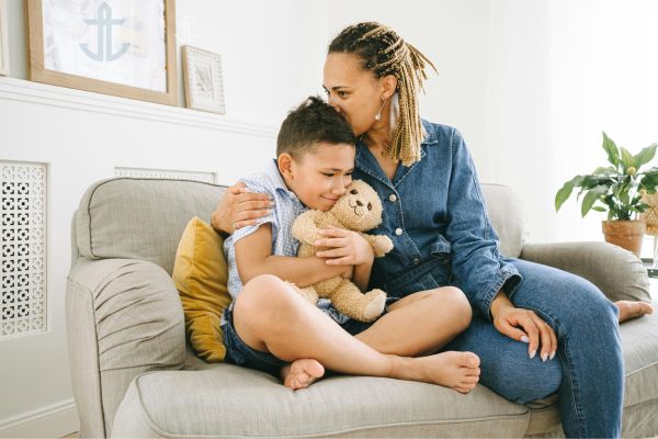 A caregiver holding a child closely on a couch, offering comfort and emotional safety during a moment of emotional regulation.
