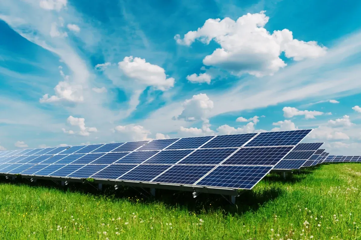 Ground-mounted solar panels arranged in a field, under a cloudy, bright blue sky