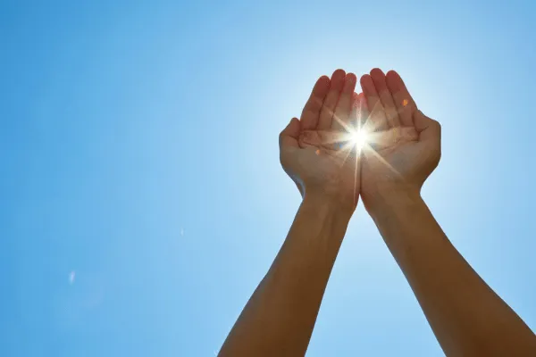 Hands held up to sky with sun shining through