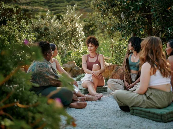  A diverse group of women sitting in a circle on cushions in a natural, outdoor setting discussing about wellness and business