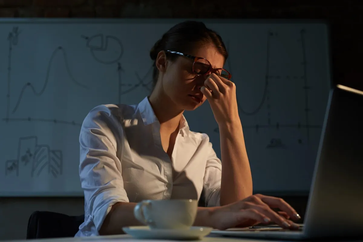tired businesswoman in glasses rubs her eyes while working late on a laptop