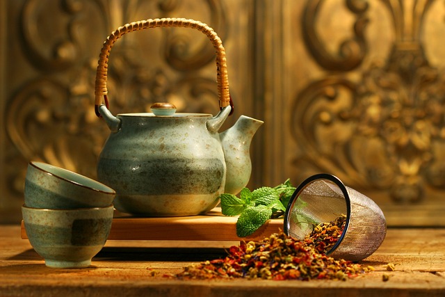 Steaming cup of tea next to a pot surrounded by loose tea leaves and petals