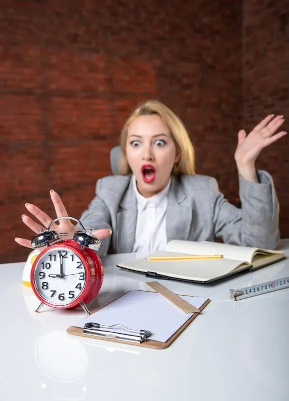 L’image montre une femme, visiblement stressée ou surprise, assise à un bureau.
