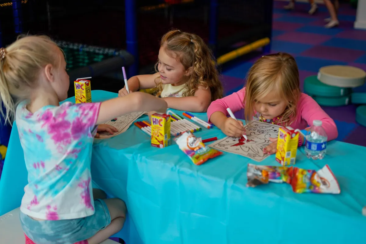 Three girls sitting at a table and coloring inside Wild Child indoor playground in Bastrop, TX