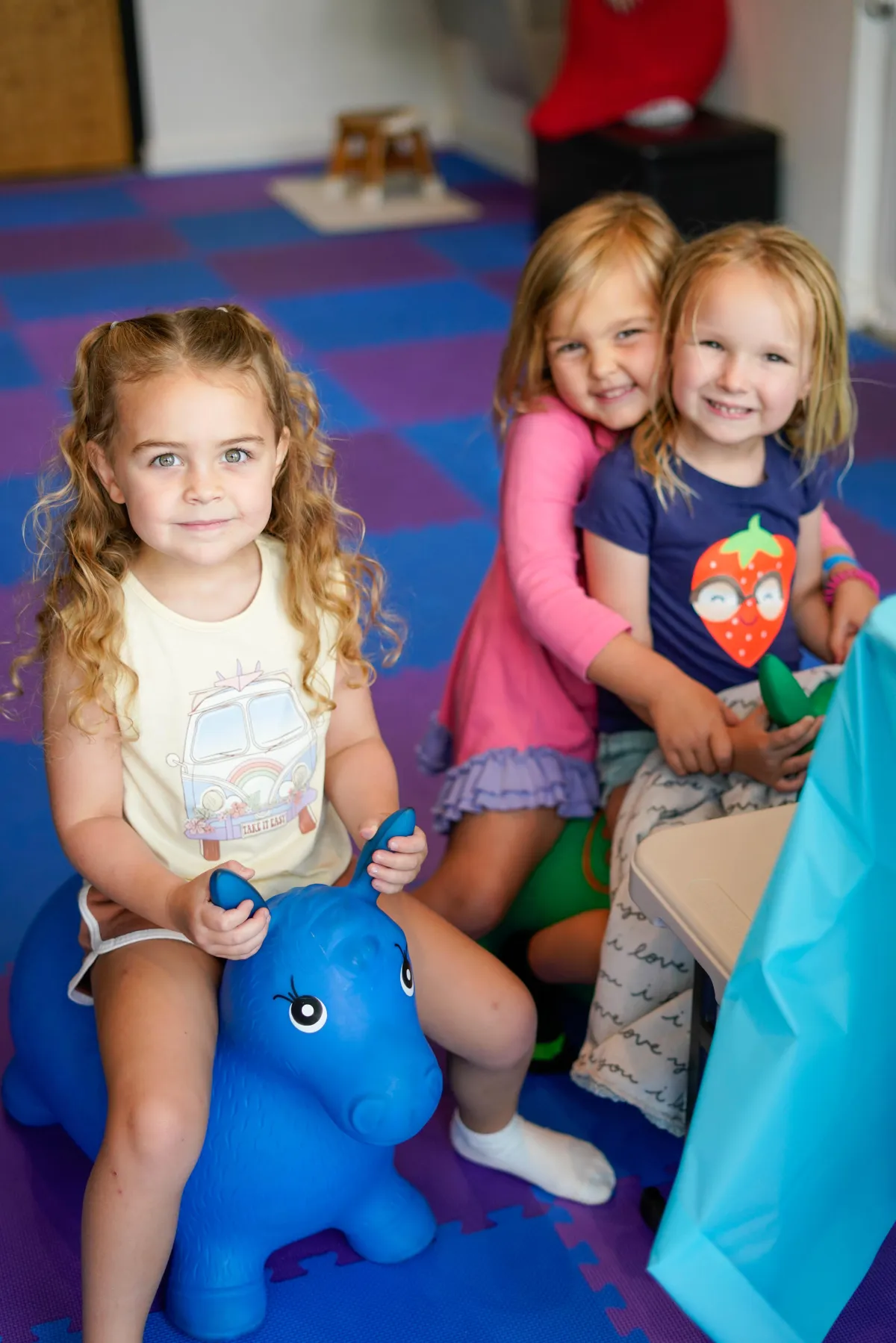 Three girls sitting on a toy and smiling inside Wild Child indoor playground in Bastrop, TX