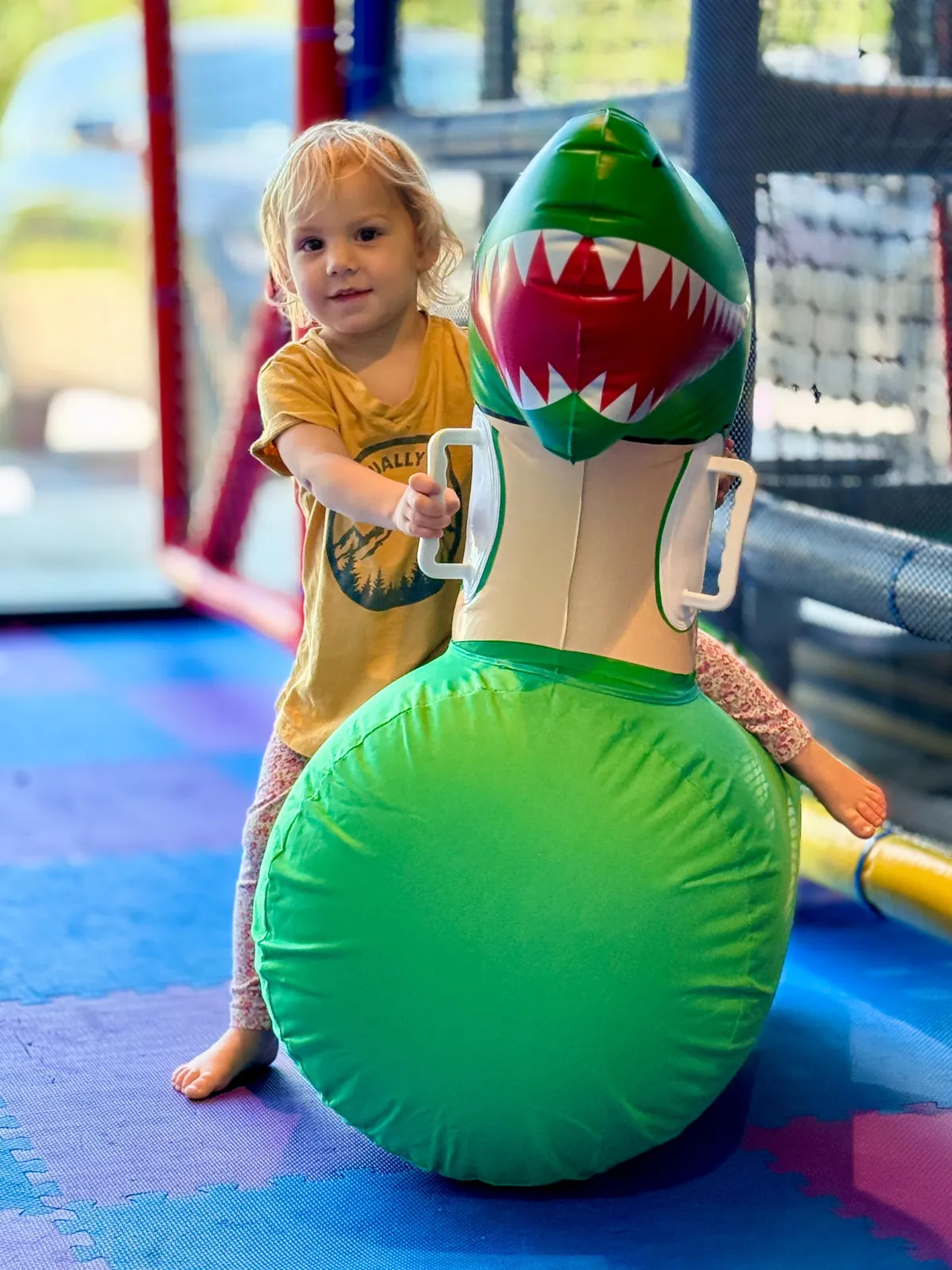 Young girl bouncing on an inflatable dinosaur toy at Wild Child indoor playground in Bastrop, TX