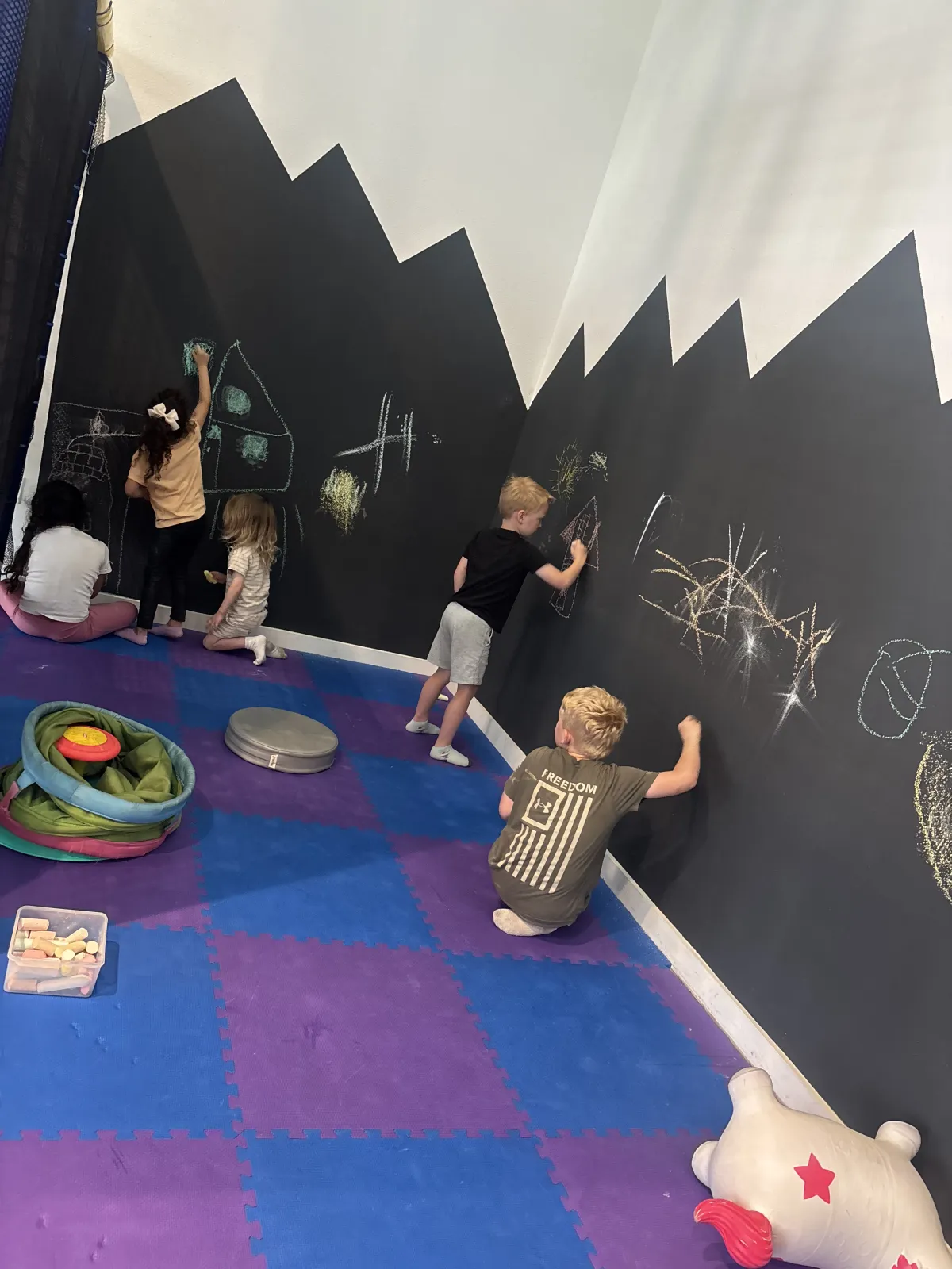 Kids drawing on a chalkboard wall at Wild Child indoor playground in Bastrop, TX