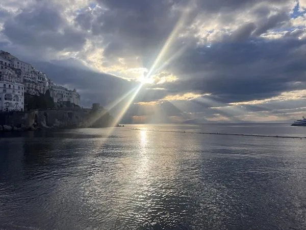 Sunlight breaking through clouds over calm water, symbolizing reflection and hope.