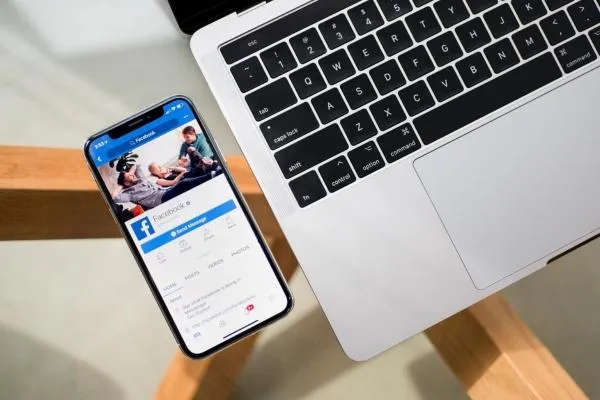 iphone and a laptop on a glass table with the facebook app open 