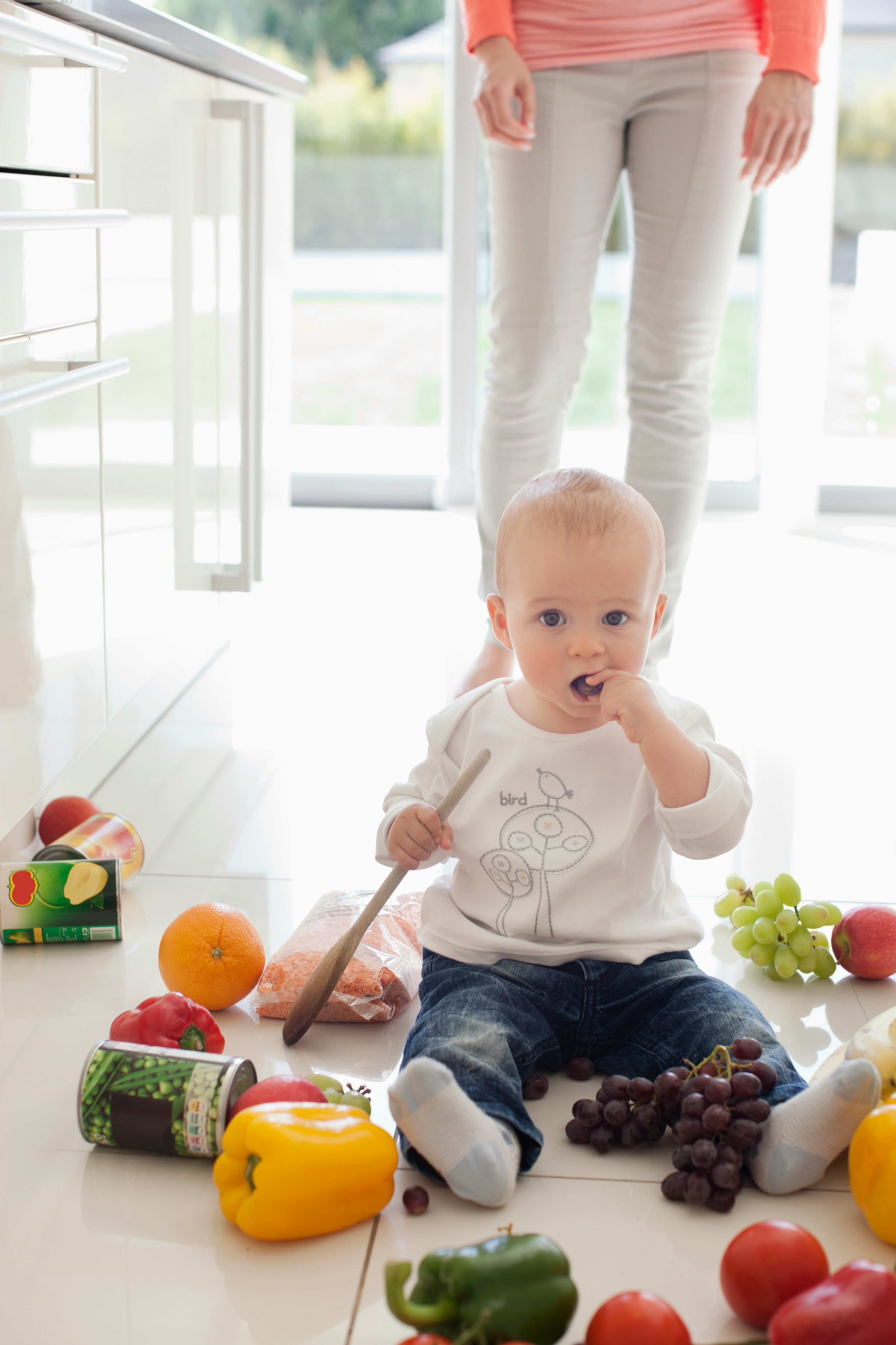 baby sitting on floor surrounded by groceries eating a grape