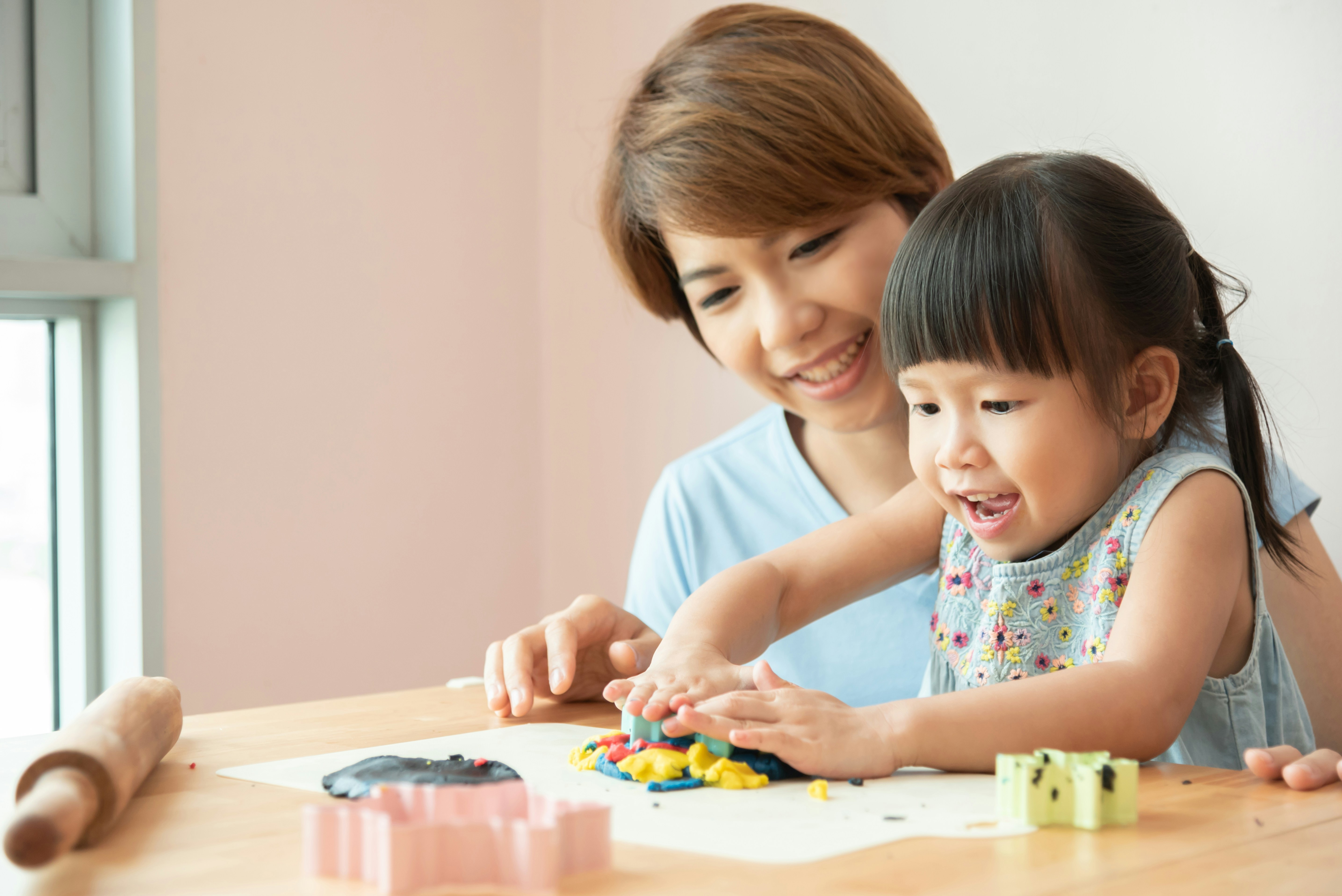 Child playing with coloured dough and Adult woman watching 