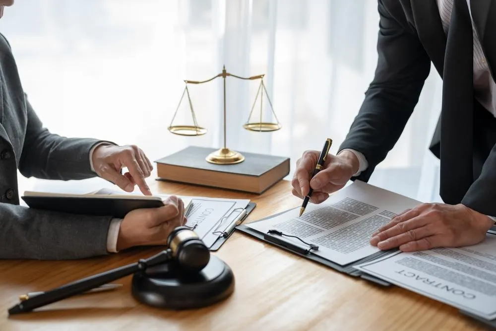 A real estate professional signing a contract with a pen on a desk filled with documents.