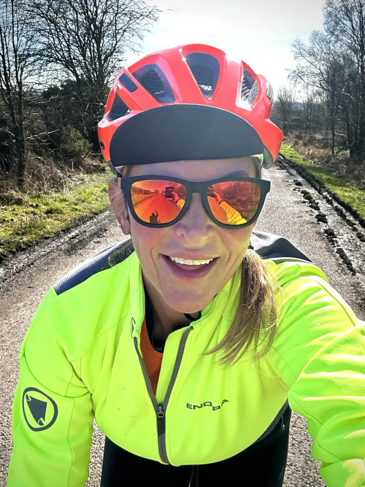 Helen cycling in Northumberland, smiling to camera wearing a bright yellow jacket and red helmet.