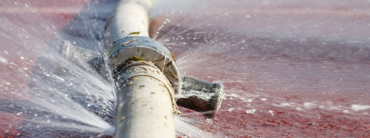 Close-up of a burst water pipe spraying water in multiple directions, illustrating a typical plumbing emergency that requires immediate professional repair.