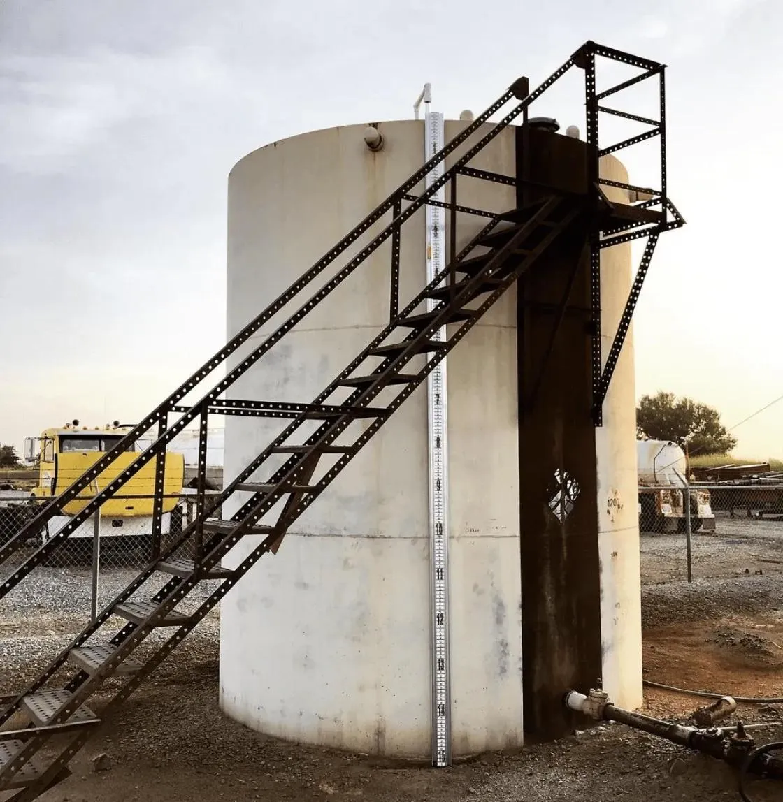 A cylindrical white storage tank with attached stairways and external level boards for accurate measurement of liquid levels. This design is optimal for sectors like construction, chemical storage, or food processing.
