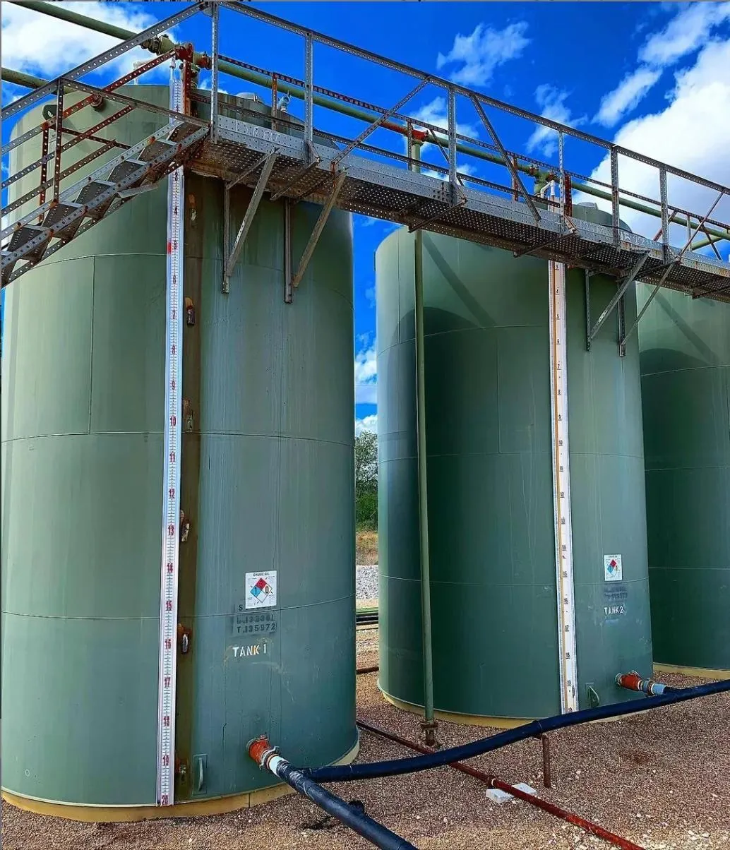 Green vertical storage tanks fitted with metal walkways and external float level gauges for precision liquid level tracking. These tanks are well-suited for agricultural water storage or fuel inventory management.